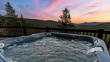 Un bain à remous avec une terrasse en bois et une vue imprenable sur les montagnes au coucher du soleil.