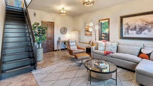 A spacious living room with a staircase, a grey sofa, a coffee table, and a large window.