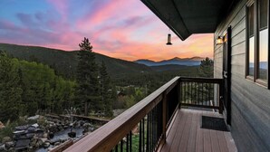 A wooden deck with a view of a mountainous landscape and a sunset.