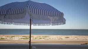 Ein Strandsonnenschirm mit Streifenmuster und Fransen, auf einem Strand unter wolkenlosem Himmel und ruhiger See.