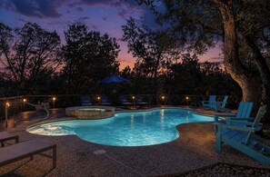 Ein Pool mit Liegestühlen und Whirlpool, umgeben von Bäumen und einem Zaun.