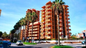 Un hôtel à plusieurs étages, doté de balcons, de palmiers et d’un panneau de signalisation indiquant un arrêt.