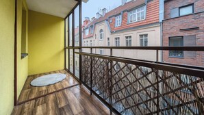 Ein Balkon mit Holzboden, gelben Wänden und Blick auf die Nachbargebäude.