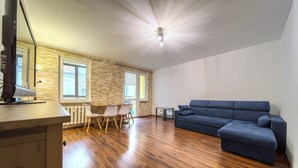 Ein geräumiger Raum mit Holzboden, einem blauen Sofa, einem Esstisch mit Stühlen und einer Steinwand.
