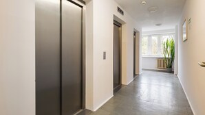 Un pasillo moderno con puerta corredera, ascensor y ventana con vista a árboles.