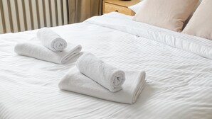 Una cama bien hecha con sábanas blancas y dos toallas enrolladas encima.