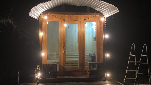 A wooden cabin with a covered porch, a ladder, and a small outdoor seating area.
