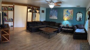 A living room with a sectional sofa, a coffee table, a bookshelf, and a ceiling fan.