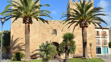 Un edificio histórico de piedra con palmeras y un jardín de flores al frente.