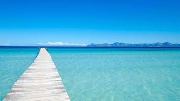 Un muelle de madera que se adentra en aguas turquesas cristalinas, con una cadena montañosa al fondo.