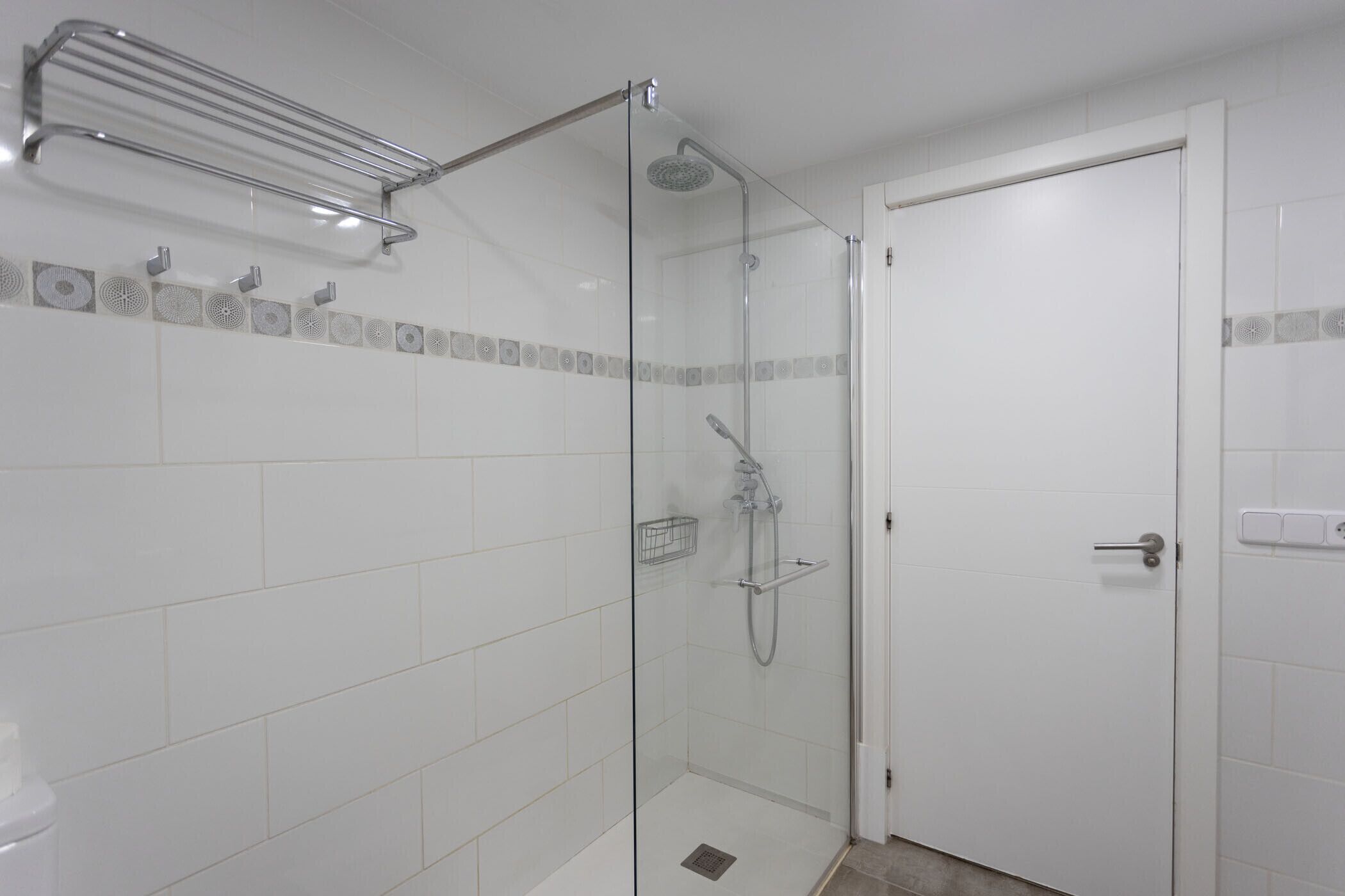 A glass-enclosed shower with a handheld showerhead and a towel rack.
