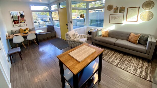 A modern living room with a dining area, a sofa, a coffee table, and a large window providing natural light.