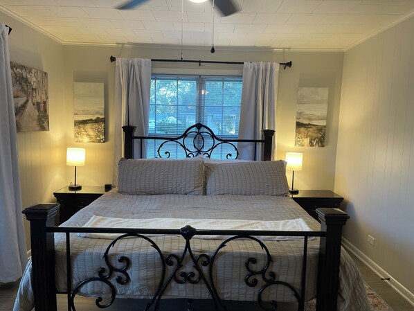 A neatly made bed with a metal frame, two bedside lamps, and a window with curtains.
