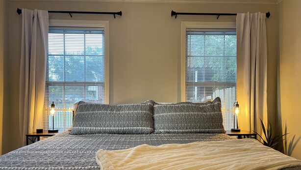 A bedroom with a large bed, two bedside lamps, and a window with blinds.