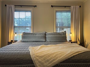A bedroom with a large bed, two bedside lamps, and a window with blinds.