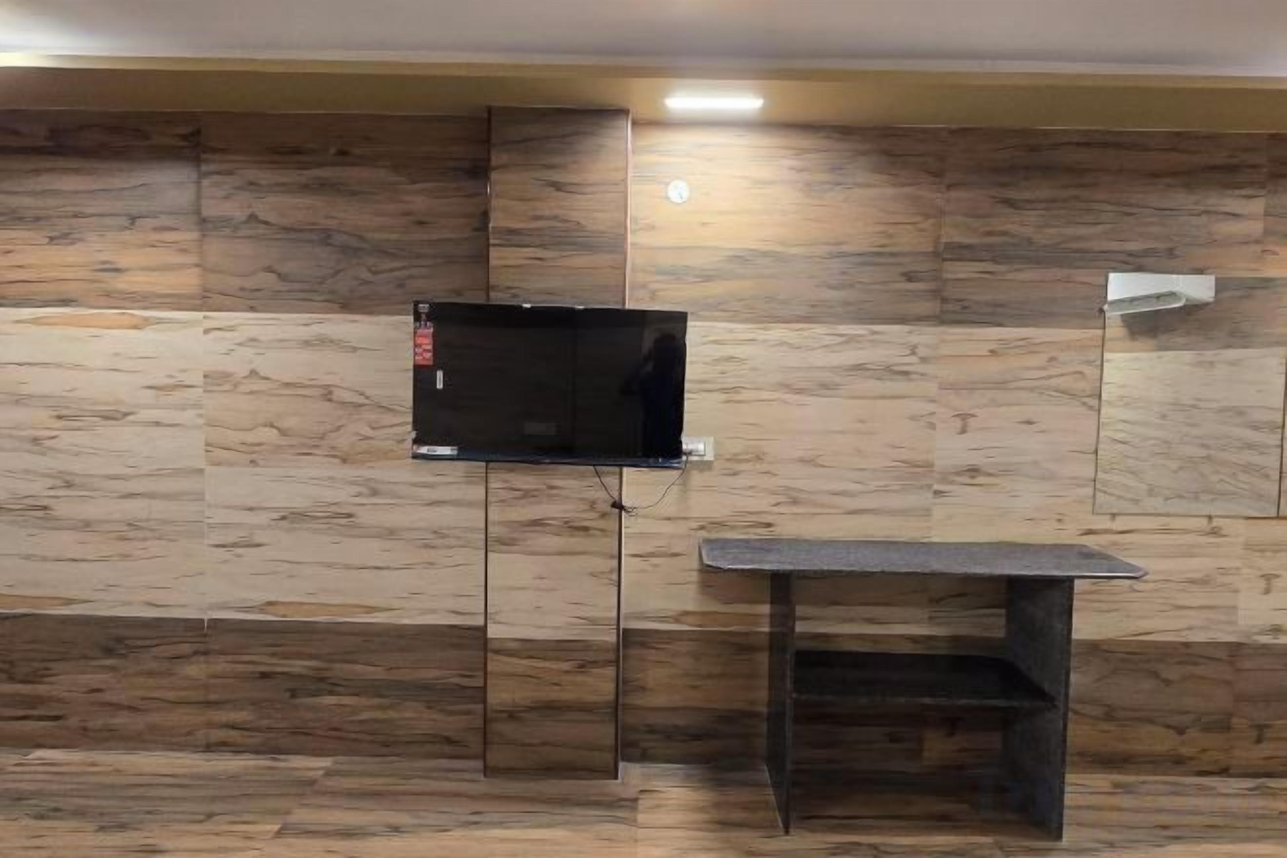 A room with a television mounted on a wall, a small table, and a bench.