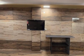 Una habitación con una televisión montada en la pared, una mesita y un banco.