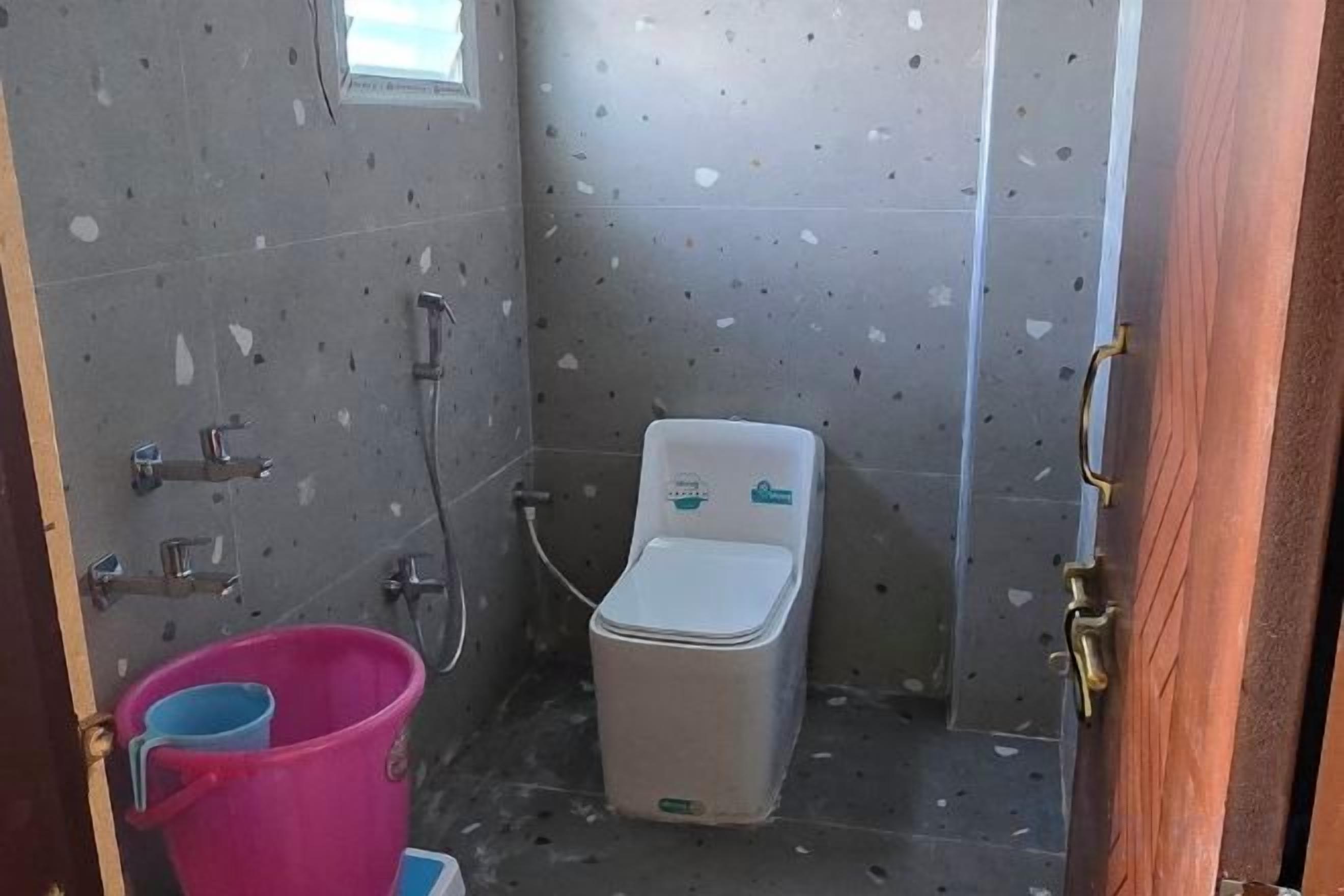 A small bathroom with a toilet, a shower, and a bucket.