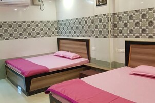 Quarto de hotel com duas camas, cada uma com cabeceira de madeira e roupa de cama rosa. O quarto possui um revestimento de azulejos e uma pequena mesa de cabeceira.