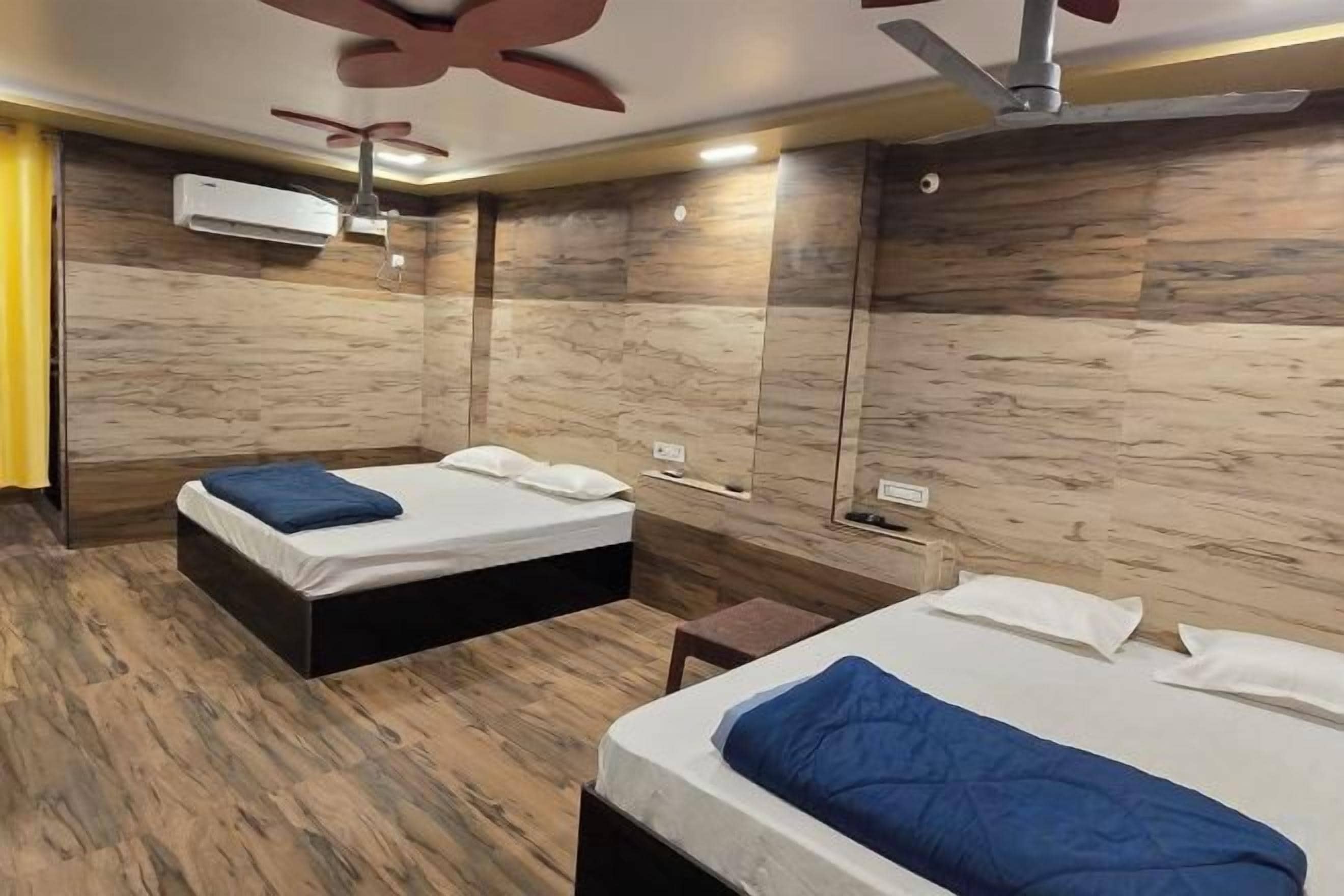 Quarto de hotel com duas camas, um ventilador de teto e piso de madeira.