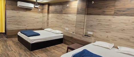 Quarto de hotel com duas camas, um ventilador de teto e piso de madeira.