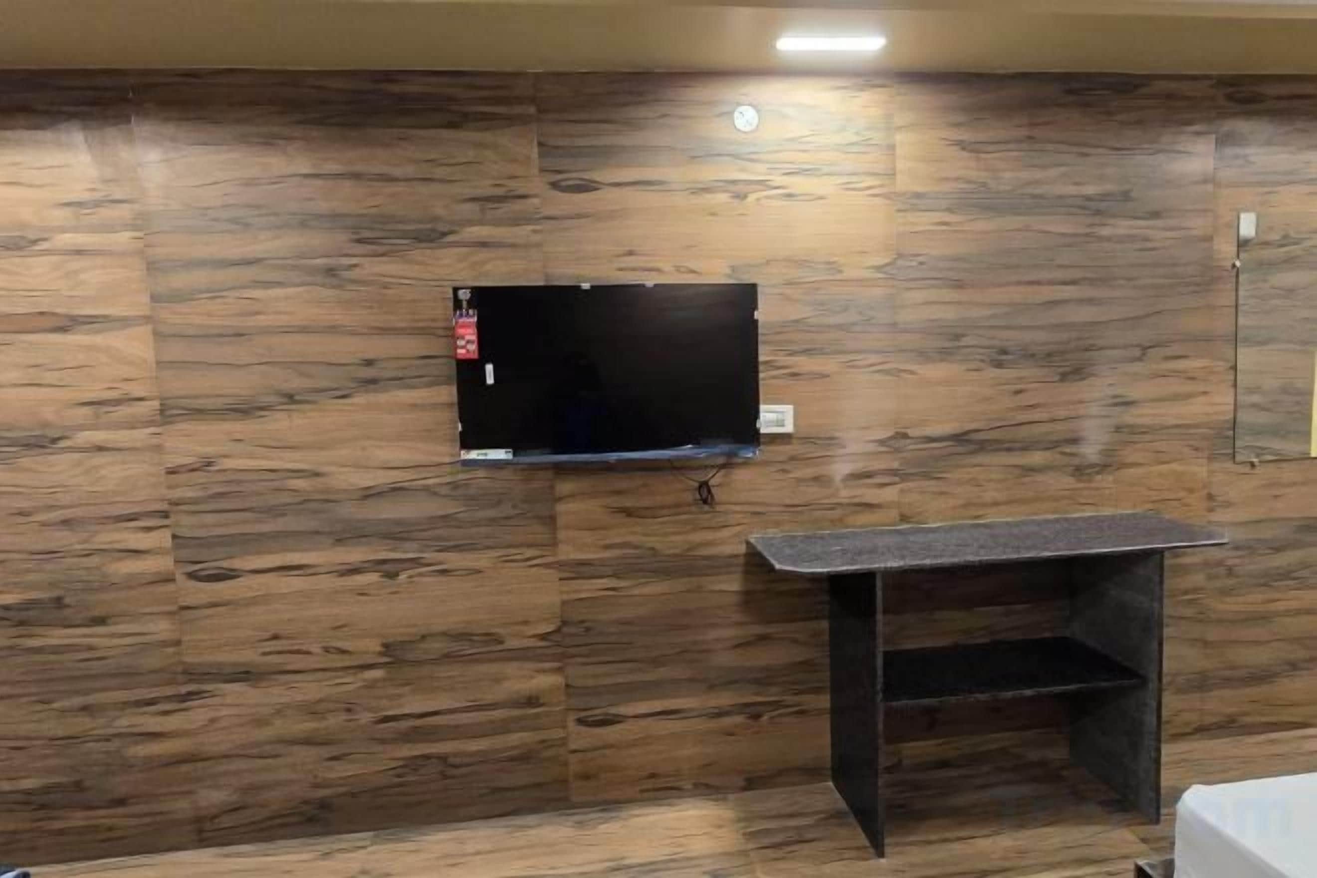 Een kamer met een wandbeugel voor een flatscreen-tv aan een houten wand, een klein zwart tafeltje en een stopcontact.