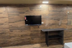 A room with a mounted flat-screen TV on a wooden wall, a small black table, and a power outlet. - Sree Mukhyaprana Residency (Mantralayam)