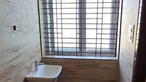Un baño con pared de mármol, un lavamanos blanco y una ventana con barrotes.