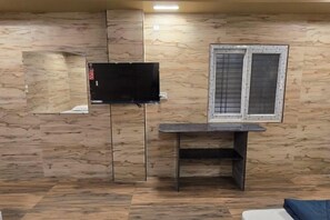 Una habitación con televisión montada en la pared, una ventana con marco metálico y una mesita.