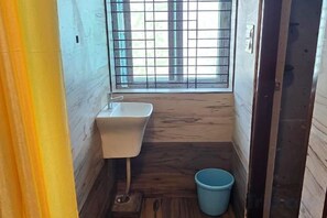 Un baño pequeño con un lavamanos, un cubo azul y una ventana con barrotes.