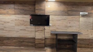 Una habitación con una televisión de pantalla plana montada en la pared, una mesita pequeña y suelo de madera.