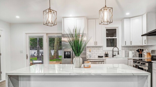 A modern kitchen with white cabinets, a large island with seating, and pendant lighting. - Cozy Ranch by the Lake w/Hot Tub in the Mountains (Albrightsville)