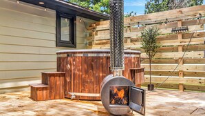 A wood-burning stove with a chimney, a wooden deck, and a wooden fence in the background. - Cozy Ranch by the Lake w/Hot Tub in the Mountains (Albrightsville)