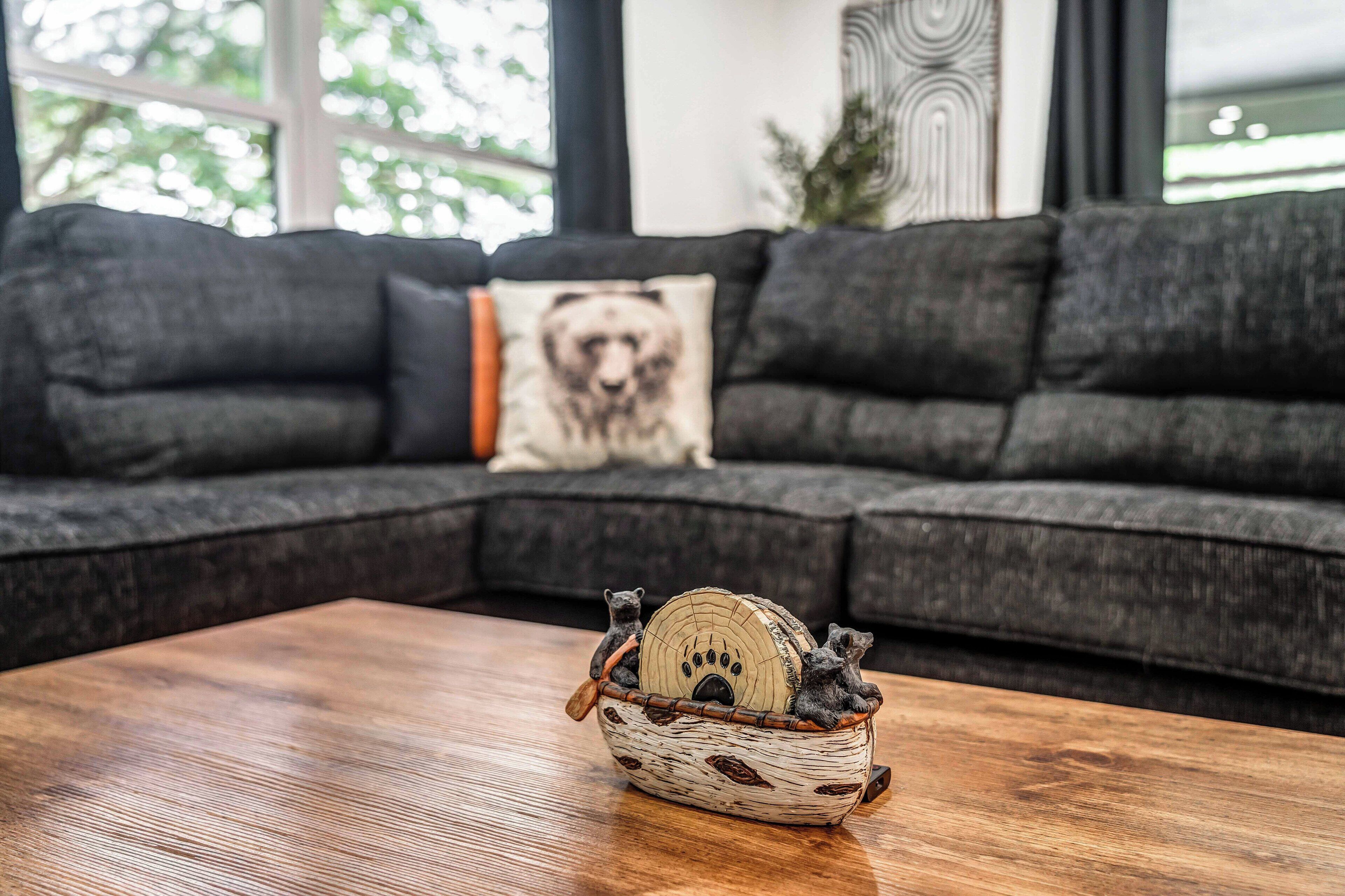 Una sala de estar moderna con un sofá seccional gris oscuro, una mesa de centro de madera y una cesta decorativa con figuritas de osos.