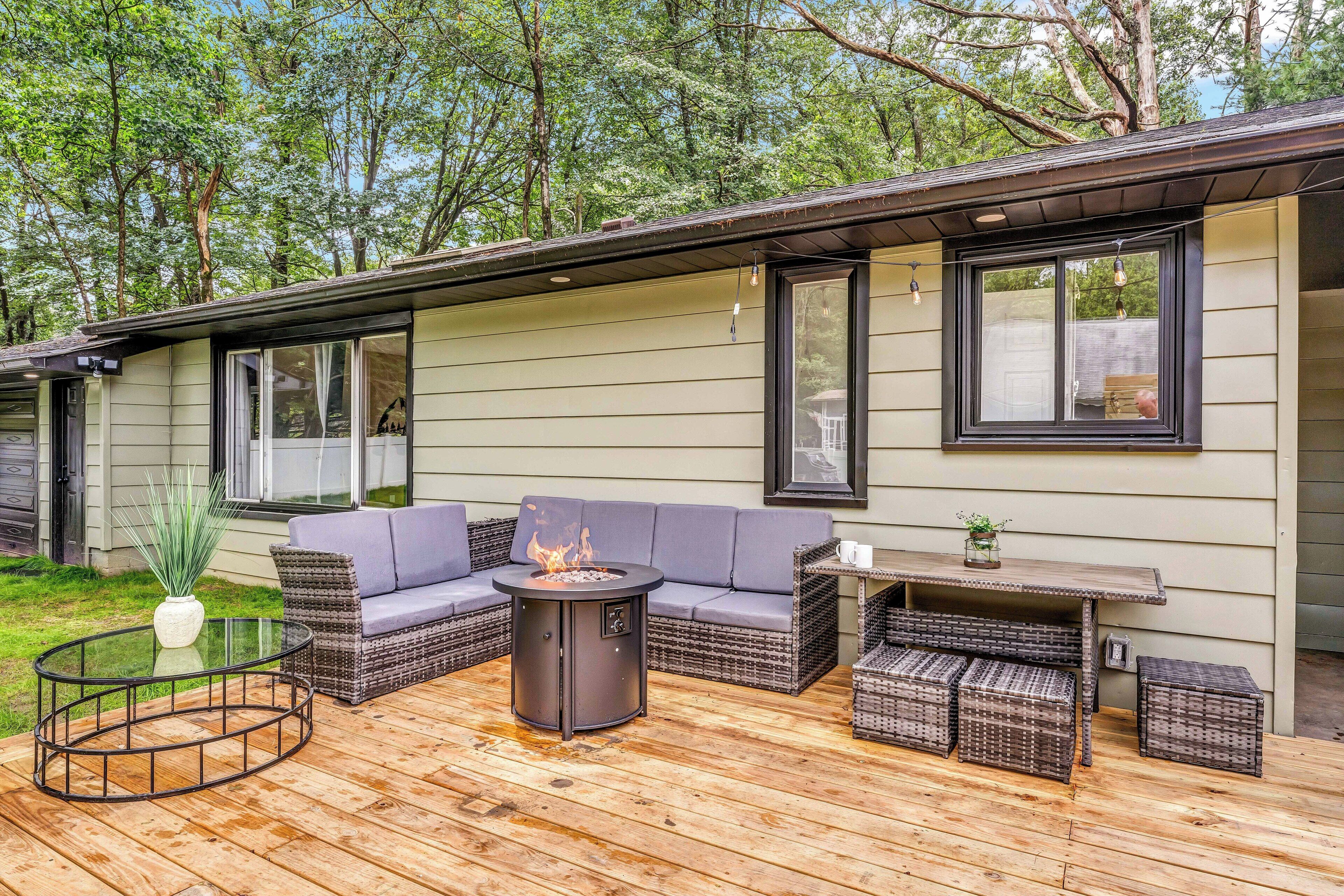 Een terras met een ronde tafel, een vuurkorf, rieten meubels en uitzicht op een huis.