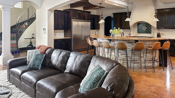 A spacious living area with a leather sofa, a kitchen with dark cabinets, a stone island, and a fireplace.