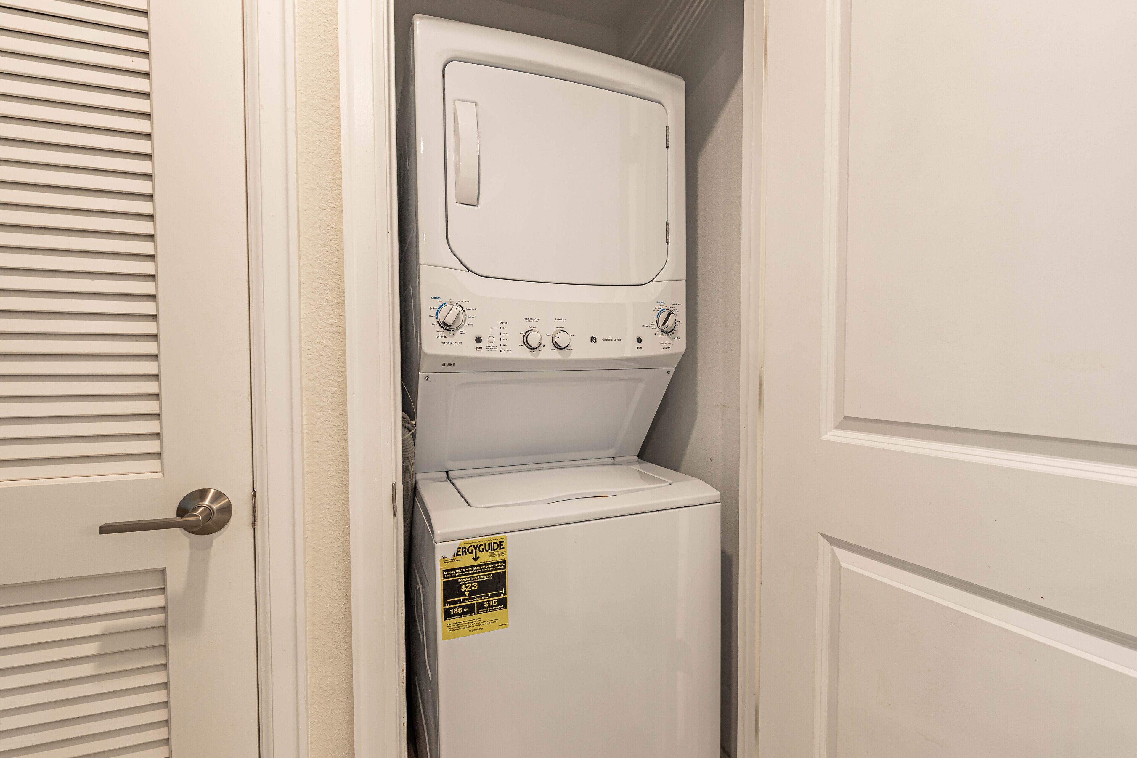 Un cuarto de lavandería con lavadora y secadora apiladas, una puerta con manija, y un letrero en la secadora.