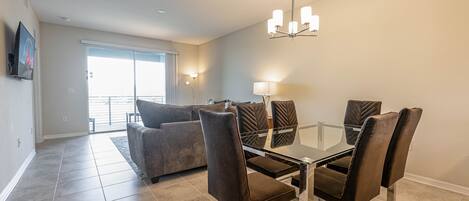 A dining area with a glass table and metal chairs, a sofa, and a chandelier.