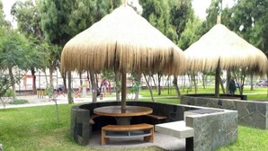 A park with thatched-roof structures, a circular seating area, and stone benches.