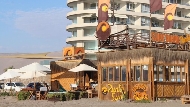 A beachfront building with a surfboard-themed restaurant named "Surfboard Rental" and a "Punta Sun Lessons" sign.