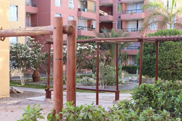 A playground with a metal swing set and a palm tree in the background.