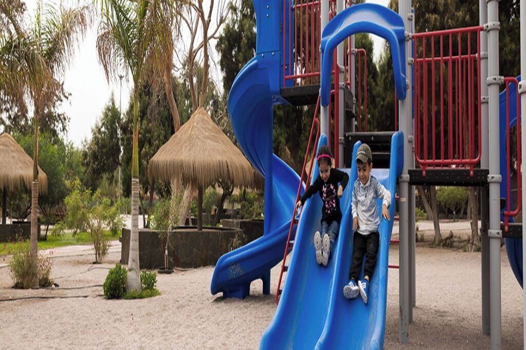 Une aire de jeux avec un toboggan bleu et une structure d’escalade.