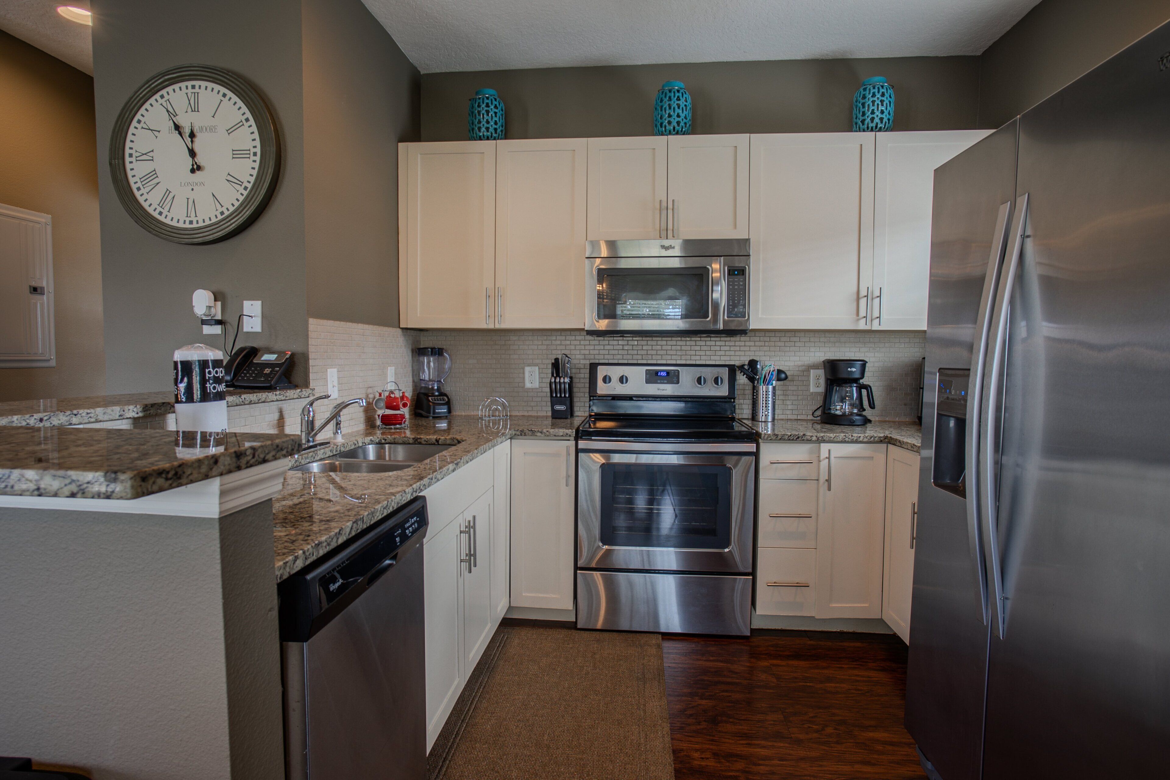A modern kitchen with stainless steel appliances, a dishwasher, a microwave, and a clock on the wall.