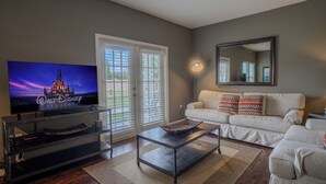 A living room with a flat-screen TV, a sofa, a coffee table, and a large mirror on the wall. - Spacious 4BR TownHome in Kissimmee, perfect for family getaways! (Kissimmee)
