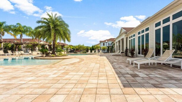 A resort pool area with palm trees, lounge chairs, and a clear blue sky. - Spacious 4BR TownHome in Kissimmee, perfect for family getaways! (Kissimmee)