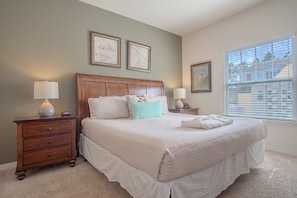 A bedroom with a large bed, two bedside tables, a nightstand, and a window with blinds.