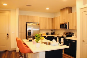 A modern kitchen with wooden cabinets, stainless steel appliances, a sink, and a bar stool.