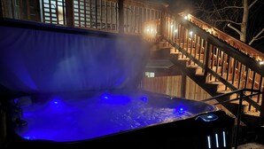 Ein Whirlpool mit blauer Beleuchtung, umgeben von einer Holzterrasse und Treppen.