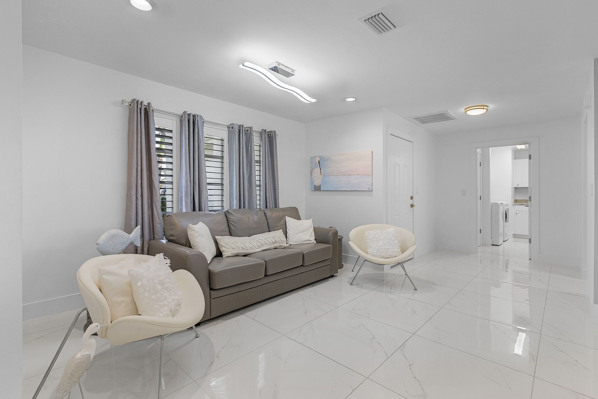 A modern living room with a grey sofa, white armchairs, and a painting on the wall.