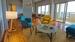 A spacious living area with a wooden floor, a round glass table, and two armchairs.
